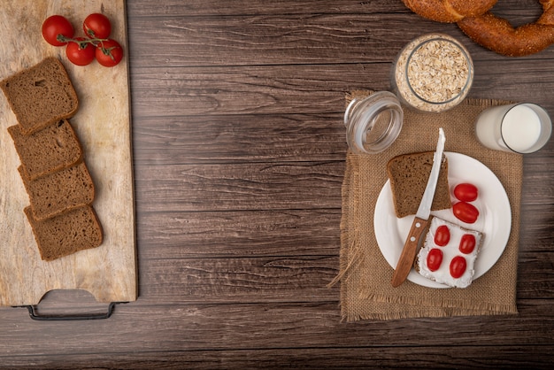 Vue de dessus du petit-déjeuner avec des tranches de pain de seigle enduites de fromage cottage et de tomates avec du lait et des flocons d'avoine sur fond de bois avec copie espace
