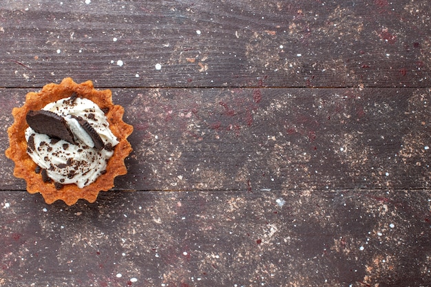 Vue de dessus du petit gâteau à la crème et au chocolat isolé sur brun en bois, gâteau biscuit cuire