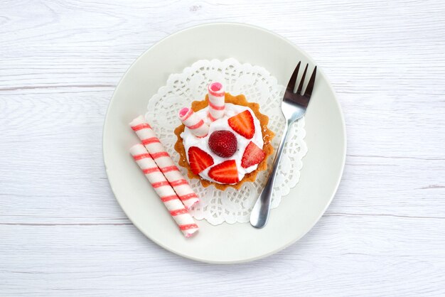 Vue de dessus du petit gâteau avec de la crème et des fraises en tranches à l'intérieur de la plaque sur blanc, gâteau aux fruits berry sucre sucré