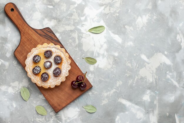 Vue de dessus du petit gâteau avec du sucre en poudre et des fruits sur la lumière, gâteau cuire tarte sucrée