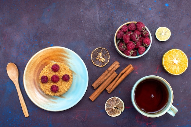 Vue de dessus du petit gâteau rond avec des framboises fraîches à l'intérieur de la plaque avec des fruits cannelle sur la surface sombre