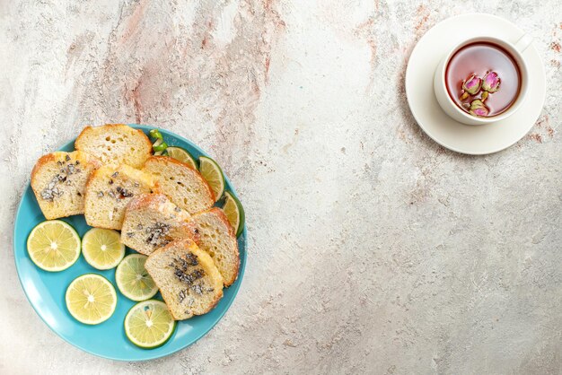 Vue de dessus du plat avec une tasse de thé assiette bleue du gâteau et du citron vert en tranches et une tasse de thé noir sur la table