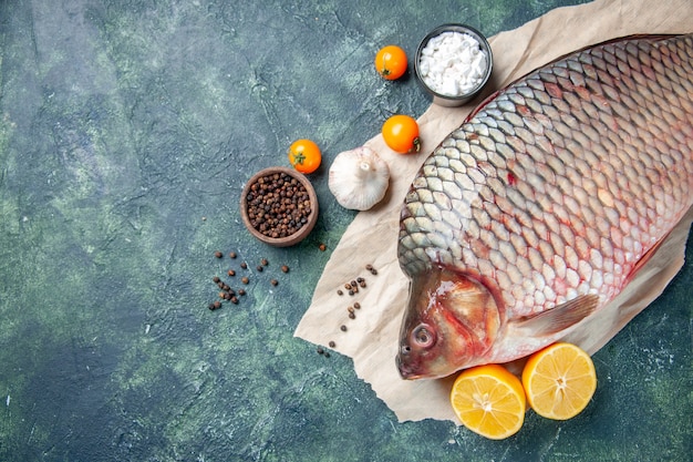 Vue de dessus du poisson cru frais avec du poivre et du citron sur fond bleu foncé