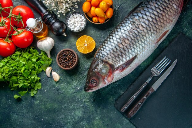 Vue de dessus du poisson cru frais avec des kumquats et des verts sur fond sombre