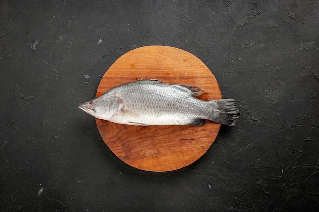 Vue de dessus du poisson cru frais sur une planche de bois ronde sur un espace libre de table noire