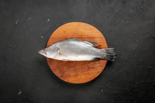 Vue de dessus du poisson cru frais sur une planche de bois ronde sur un espace libre de table noire