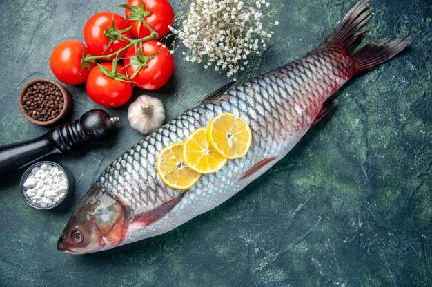 Vue de dessus du poisson cru frais avec des tomates et du citron sur fond bleu foncé