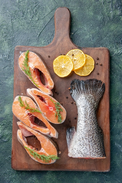 Photo gratuite vue de dessus du poisson cru frais tranches de citron poivre vert sur planche à découper en bois sur la table des couleurs de mélange sombre