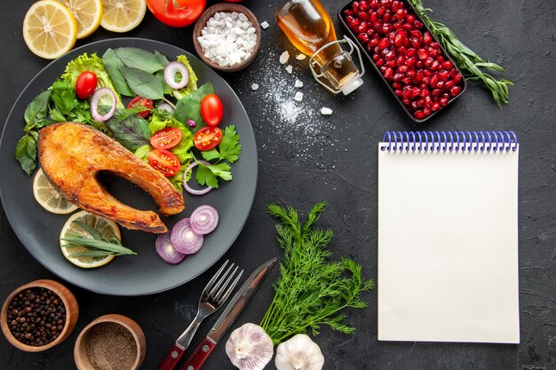 Vue de dessus du poisson cuit savoureux avec des légumes frais sur la table sombre