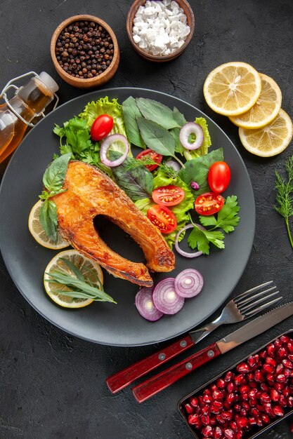 Vue de dessus du poisson cuit savoureux avec des légumes frais sur la table sombre