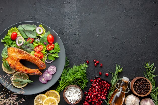 Vue de dessus du poisson cuit savoureux avec des légumes frais sur la table sombre