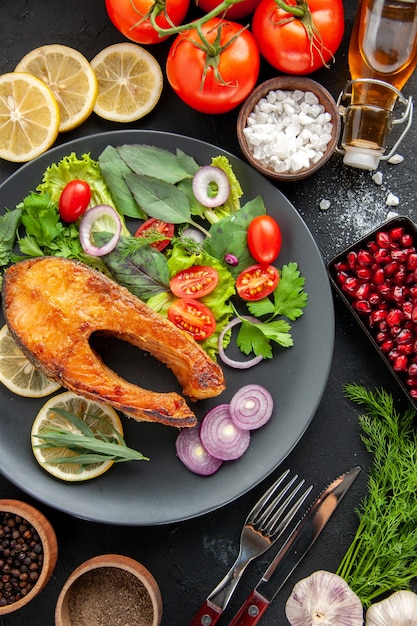 Vue de dessus du poisson cuit savoureux avec des légumes frais sur la table sombre