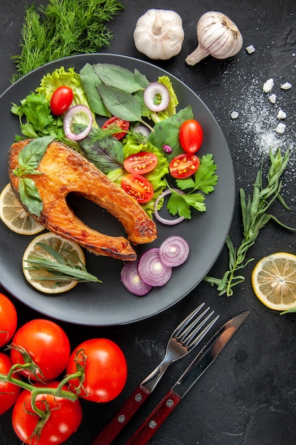 Vue de dessus du poisson cuit savoureux avec des légumes frais sur la table sombre