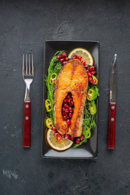 Photo gratuite vue de dessus du poisson cuit savoureux avec des légumes verts et des tranches de citron à l'intérieur de la casserole sur une table sombre