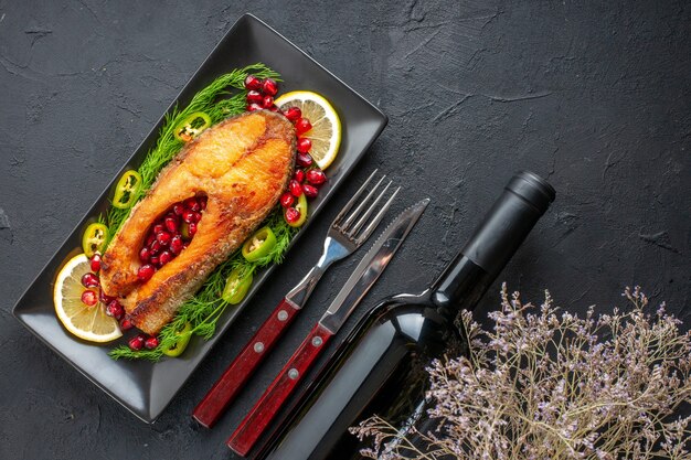 Vue de dessus du poisson cuit savoureux avec des légumes verts et des tranches de citron à l'intérieur de la casserole sur une table sombre