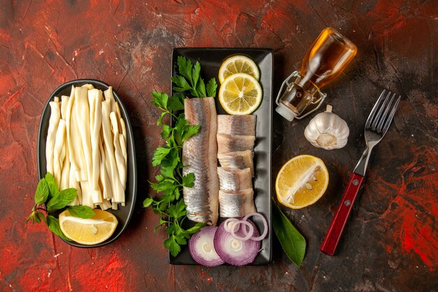 Vue de dessus du poisson frais tranché avec du citron vert et des oignons à l'intérieur d'une casserole noire sur fond sombre