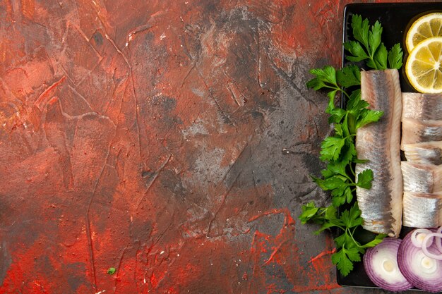 Vue de dessus du poisson frais tranché avec des légumes verts et de l'oignon à l'intérieur d'une casserole noire sur fond sombre