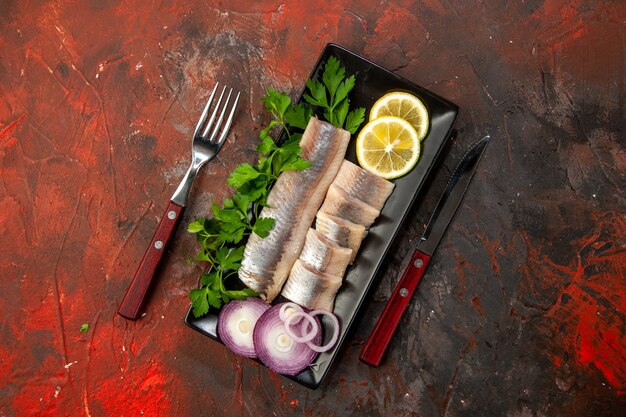 Vue de dessus du poisson frais tranché avec des légumes verts et de l'oignon à l'intérieur d'une casserole noire sur fond sombre