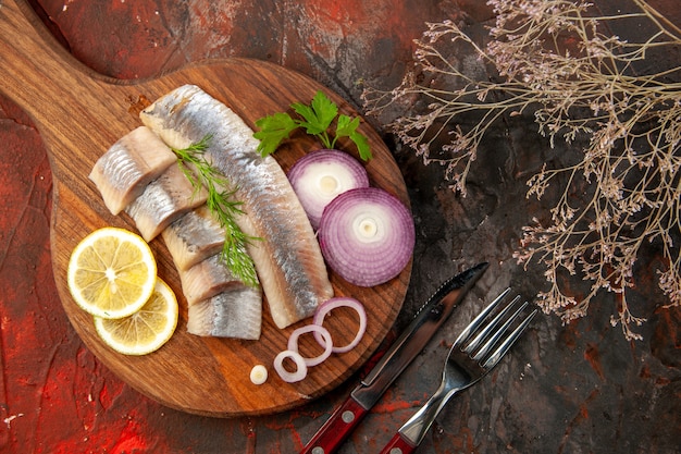 Vue de dessus du poisson frais tranché avec rondelles d'oignon et citron sur fond sombre