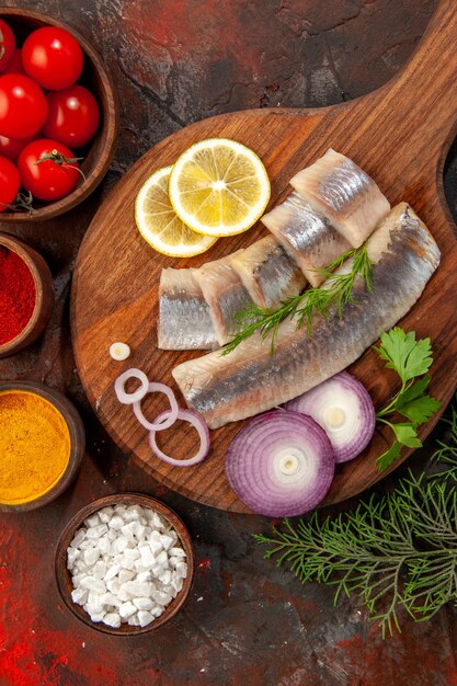 Vue de dessus du poisson frais tranché avec des tomates fraîches et des assaisonnements sur fond sombre