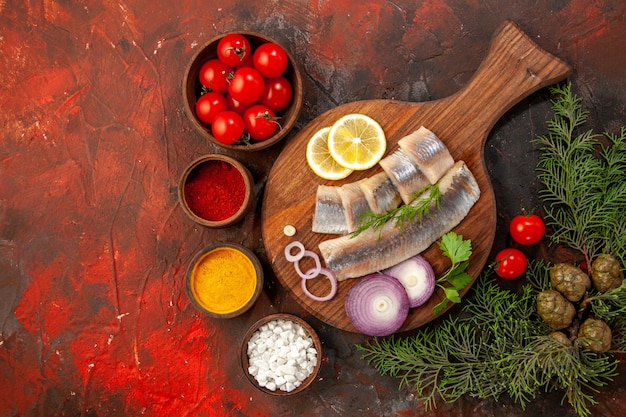 Vue de dessus du poisson frais tranché avec des tomates fraîches et des assaisonnements sur fond sombre