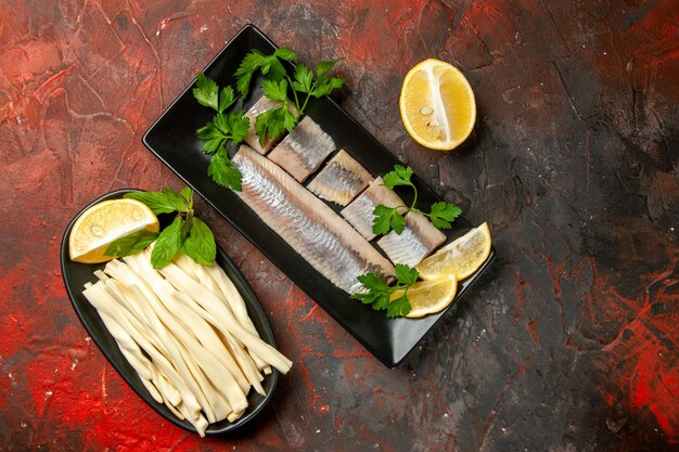 Vue de dessus du poisson frais tranché avec des verts et des morceaux de citron à l'intérieur d'une casserole noire sur fond sombre