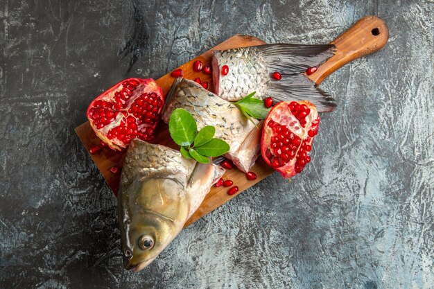 Vue de dessus du poisson frais en tranches avec des grenades sur une surface sombre