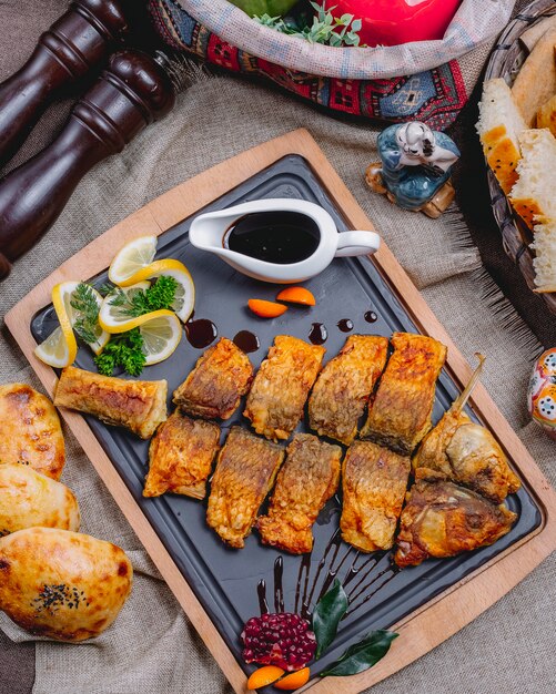 Vue de dessus du poisson frit avec tranches de citron et sauce à la grenade sur un plateau