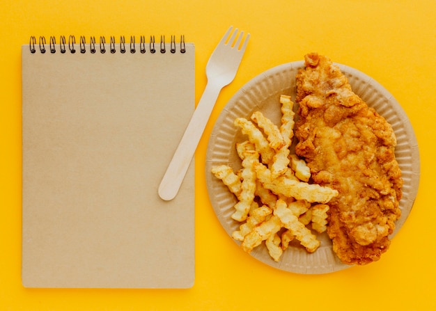 Vue de dessus du poisson-frites sur assiette avec fourchette et cahier
