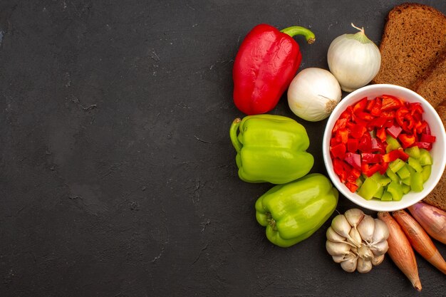 Vue de dessus du poivron tranché avec des légumes et des miches de pain noir sur un espace sombre