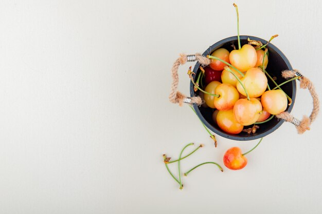 Vue de dessus du pot plein de cerises et de tiges sur le côté droit et la surface blanche avec copie espace