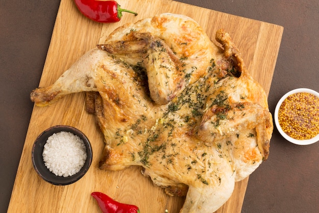 Vue de dessus du poulet cuit sur une planche à découper avec moutarde de Dijon et poivrons rouges