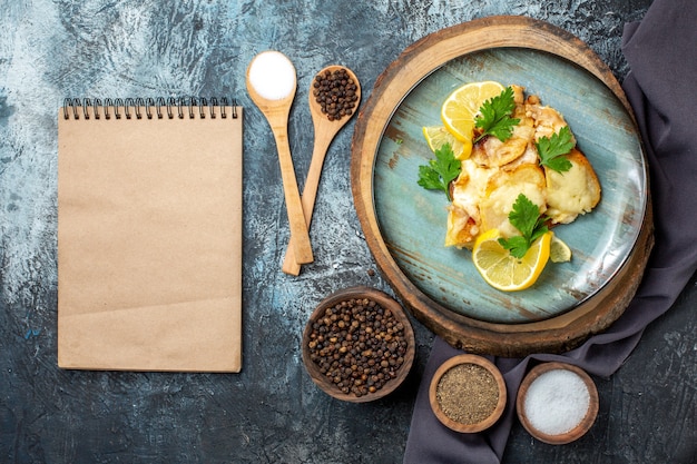 Vue de dessus du poulet avec du fromage sur la plaque sur les épices de planche de bois dans le bloc-notes de cuillères en bois sur table grise