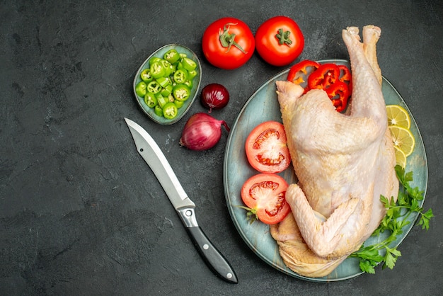 Vue de dessus du poulet frais cru à l'intérieur de la plaque avec des verts et des légumes sur fond sombre