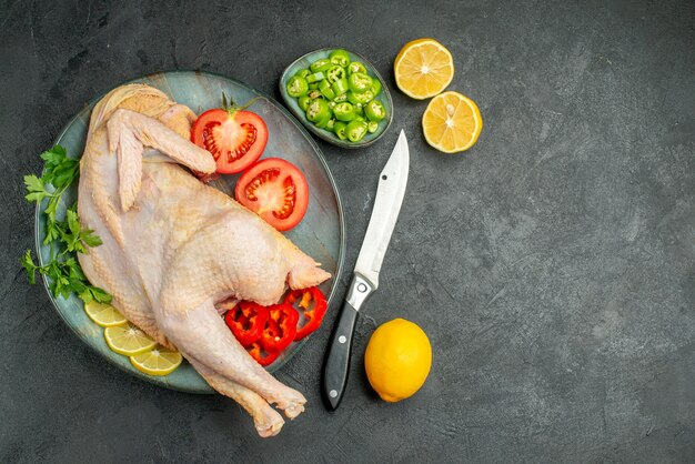 Vue de dessus du poulet frais cru à l'intérieur de la plaque avec des verts et des légumes sur fond sombre