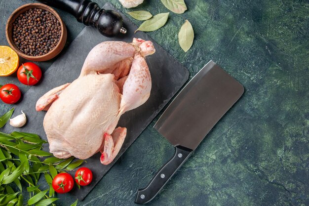 Vue de dessus du poulet frais avec des tomates et du poivre sur une surface bleu foncé