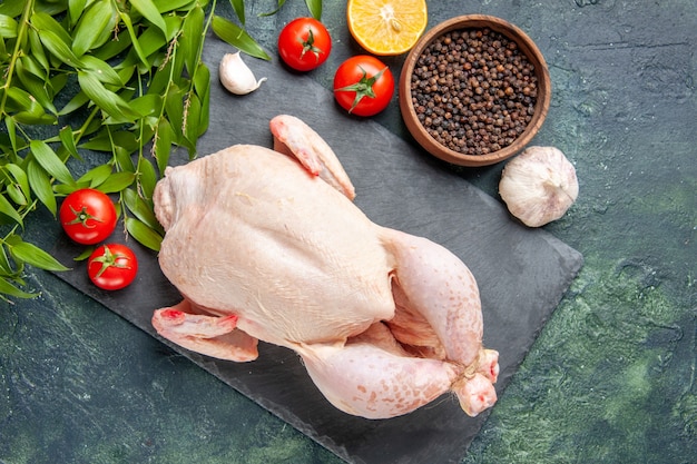 Vue de dessus du poulet frais avec des tomates et du poivre sur une surface bleu foncé