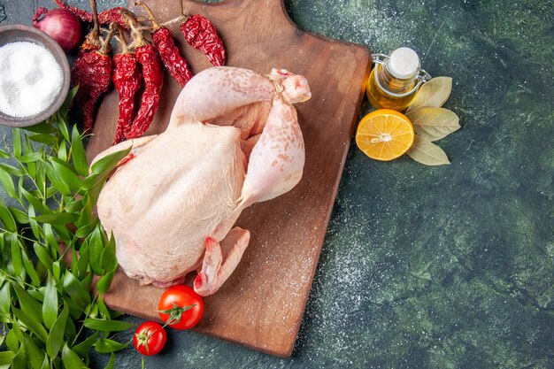 Vue de dessus du poulet frais avec des tomates rouges sur une surface bleu foncé