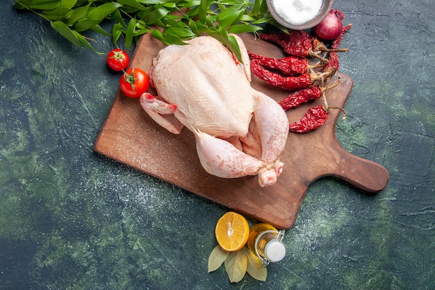 Vue de dessus du poulet frais avec des tomates rouges sur une surface bleu foncé