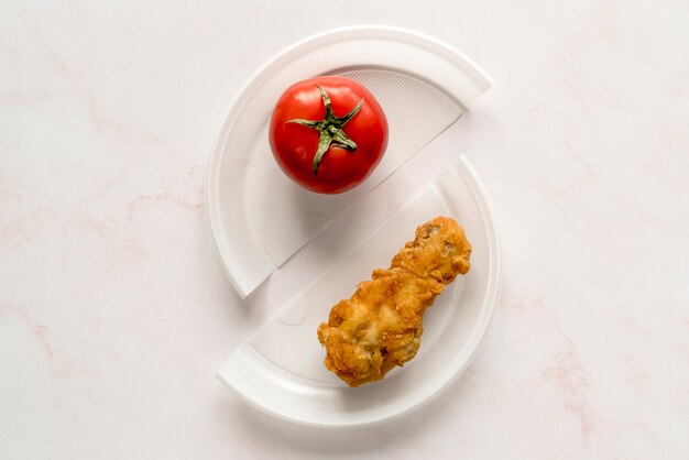 Vue de dessus du poulet frit et tomates rouges entières sur une assiette cassée