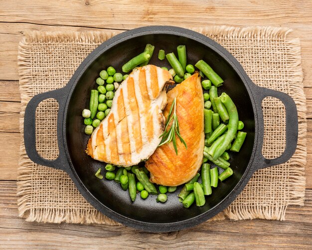 Vue de dessus du poulet grillé et des pois dans une poêle avec des herbes