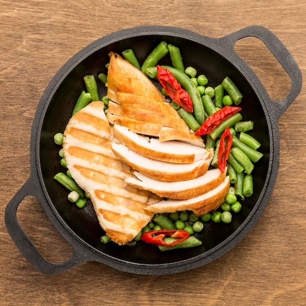 Vue de dessus du poulet grillé et des pois dans une poêle avec des piments