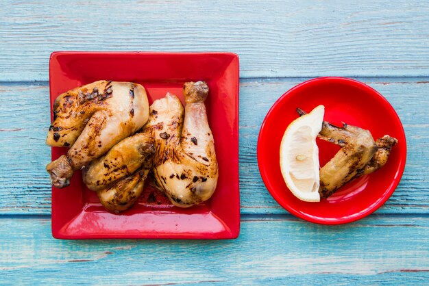 Vue de dessus du poulet grillé servi dans une assiette rouge sur une table bleue