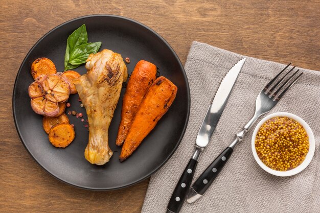 Vue de dessus du poulet et des légumes cuits au four sur une assiette avec des couverts et de la moutarde de Dijon