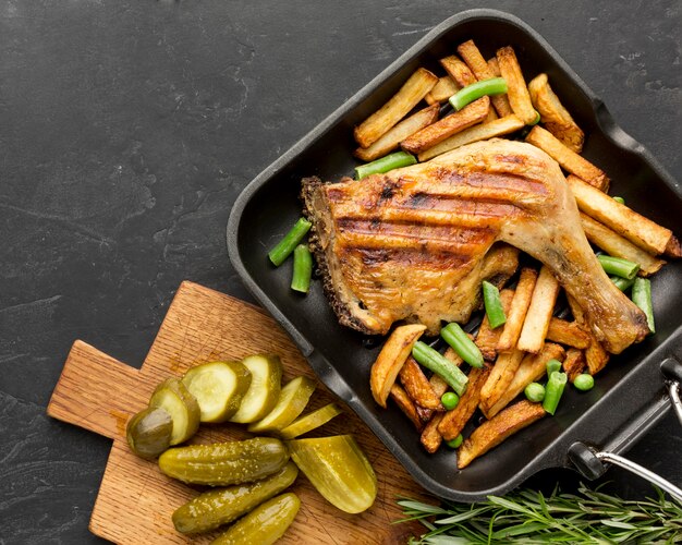 Vue de dessus du poulet et des pommes de terre au four dans une poêle avec des cornichons