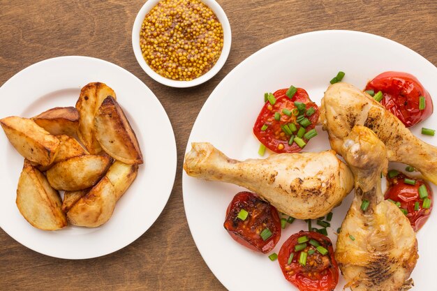 Vue de dessus du poulet et des tomates cuits au four sur une assiette avec des quartiers et de la moutarde de Dijon