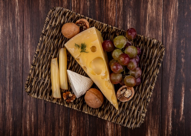 Vue de dessus du raisin avec des variétés de fromages et de noix sur un support sur un fond en bois