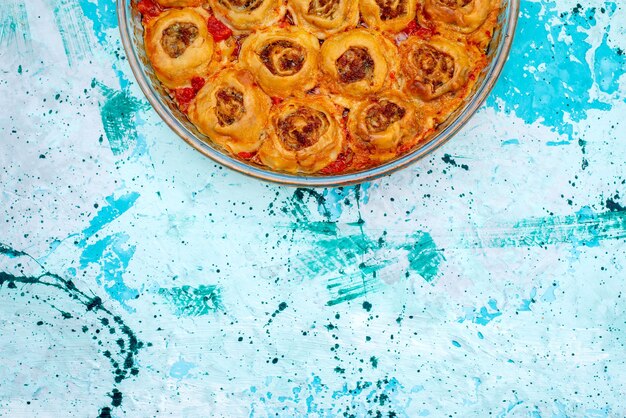 Vue de dessus du repas de pâte cuite avec de la viande hachée et de la sauce tomate à l'intérieur d'une casserole en verre sur un bureau bleu vif, cuire la pâte de viande alimentaire