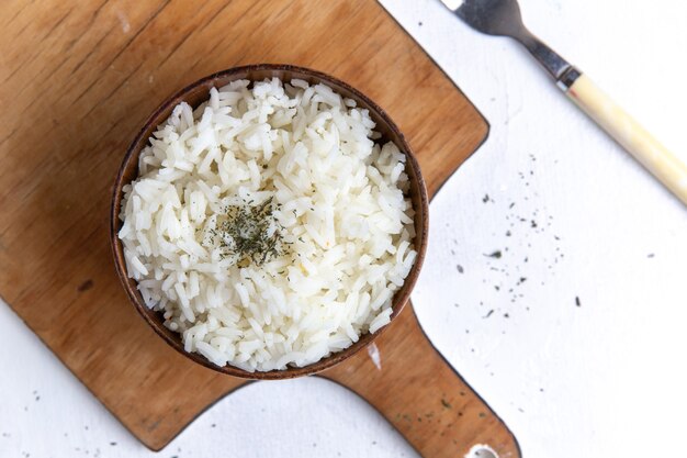 Vue de dessus du repas savoureux de riz cuit à l'intérieur du pot brun avec de l'huile sur la surface blanche