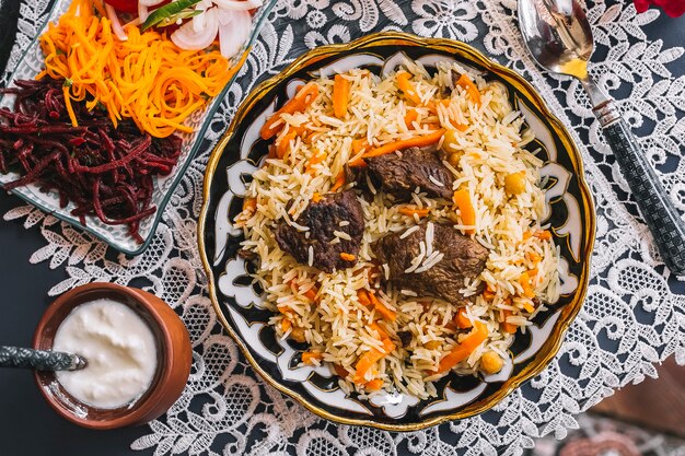 Vue de dessus du riz aux carottes cuit avec de l'agneau servi avec du yogourt et de la salade